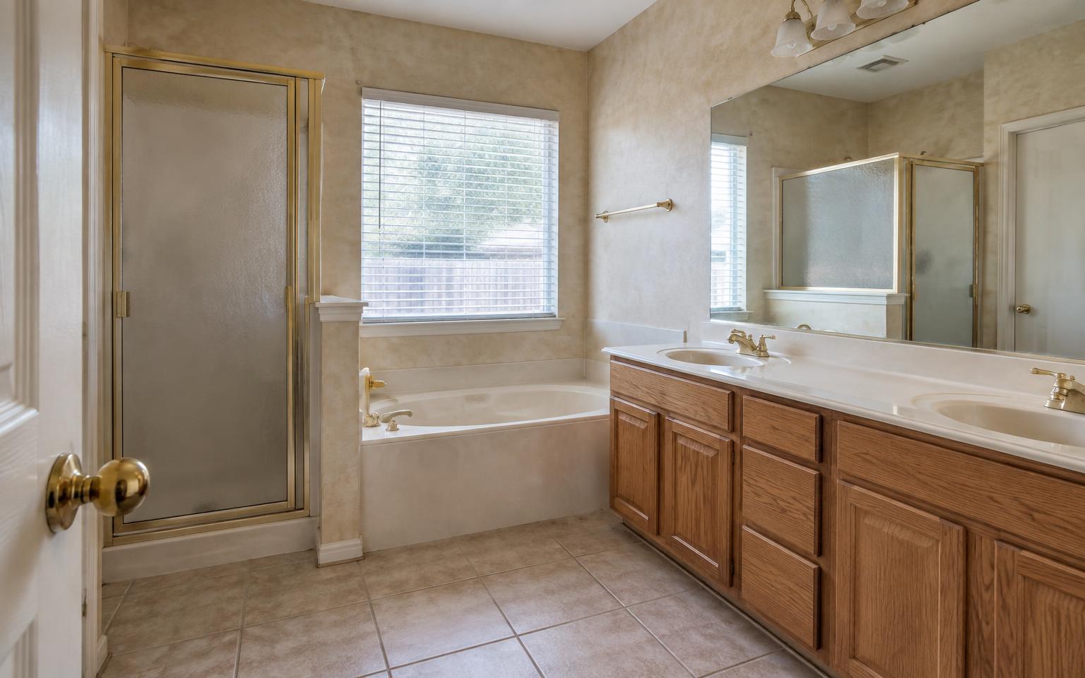 Dated primary bathroom before renovation with an enclosed shower, oak vanity, and beige tile